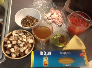 Mise en place for Mushroom ragu. From top left: porcini mushrooms, pancetta, crushed tomatoes, parmesan cheese, spaghetti, portobellos, chicken broth and a bowl holding the olive oil, garlic, rosemary and tomato paste.